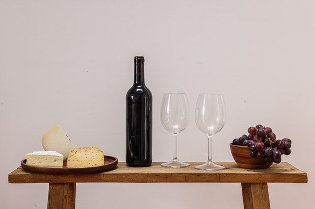 A bottle of wine with two glasses, grapes, and cheese.