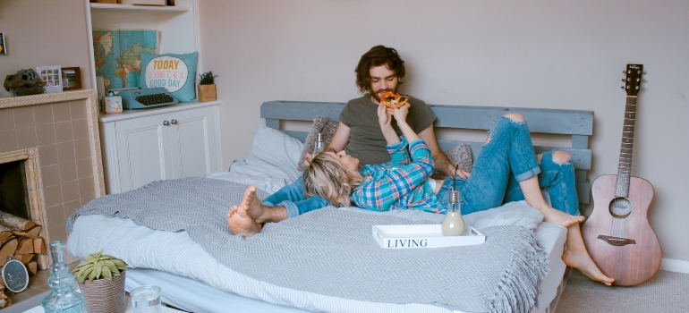A couple eating on a bed.