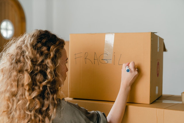 A woman writing “fragile” on a box of fragile home decor items