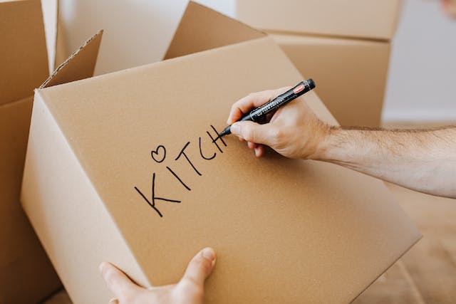 A person writing “kitchen” on a box