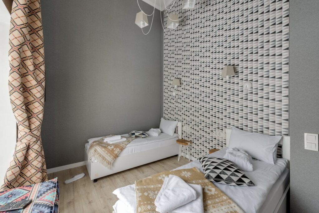 A small room with two beds and wallpaper with geometric patterns.