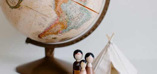 A close-up of a world globe with two wooden figurines representing cultural attire next to a white fabric teepee